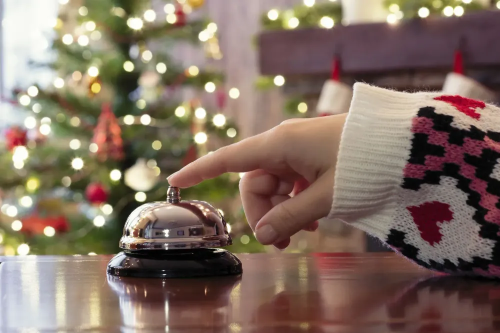 Hand ringing concierge bell at hotel desk with Christmas tree in background